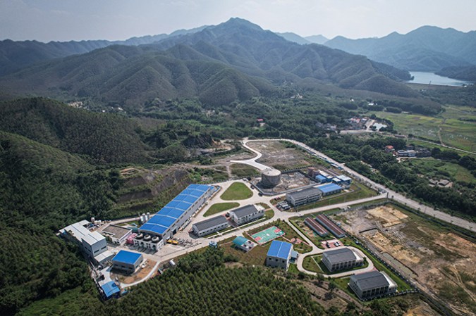 A view from above shows laboratory buildings and roadways surrounded by forested mountains.